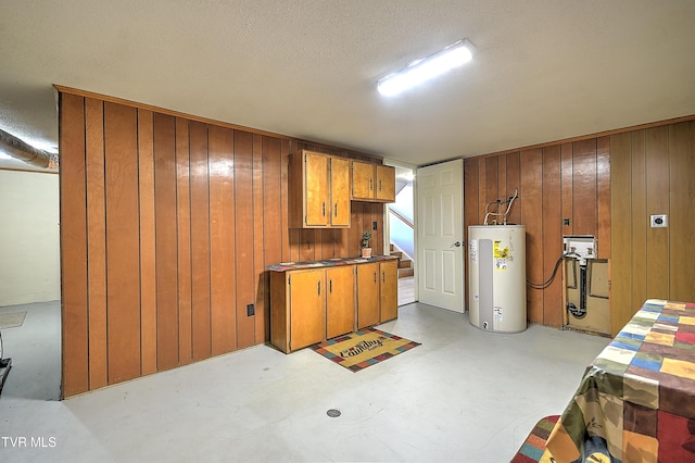 basement with a textured ceiling, water heater, and wood walls