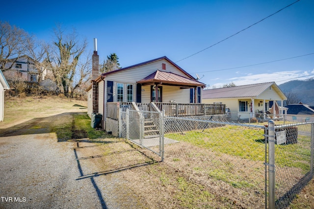 bungalow-style home featuring metal roof, a fenced front yard, covered porch, driveway, and a chimney