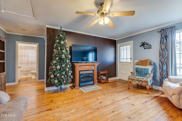 living area with a wealth of natural light, a glass covered fireplace, crown molding, and hardwood / wood-style flooring