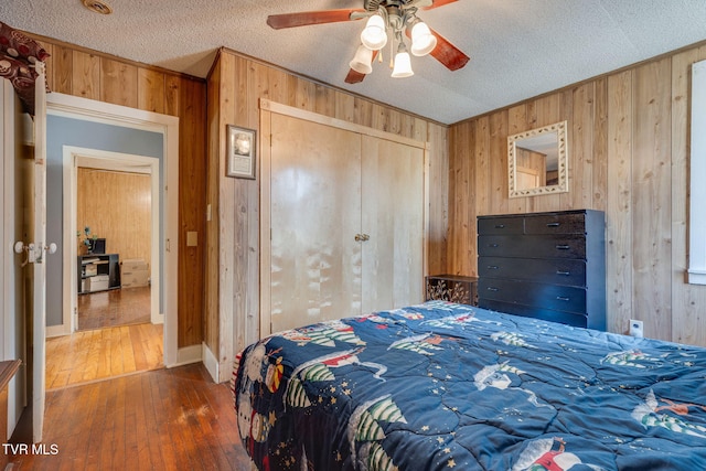 bedroom with a closet, wood-type flooring, wood walls, and a textured ceiling