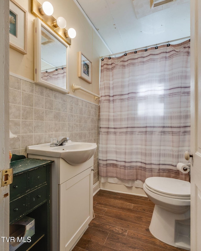 bathroom with wainscoting, toilet, wood finished floors, vanity, and tile walls