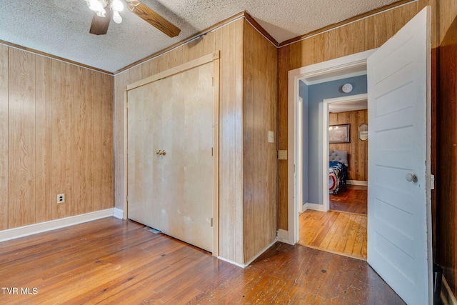 unfurnished bedroom with a textured ceiling, hardwood / wood-style flooring, wood walls, a closet, and crown molding