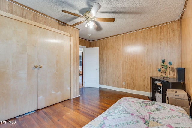 bedroom with a closet, a ceiling fan, wooden walls, a textured ceiling, and wood finished floors