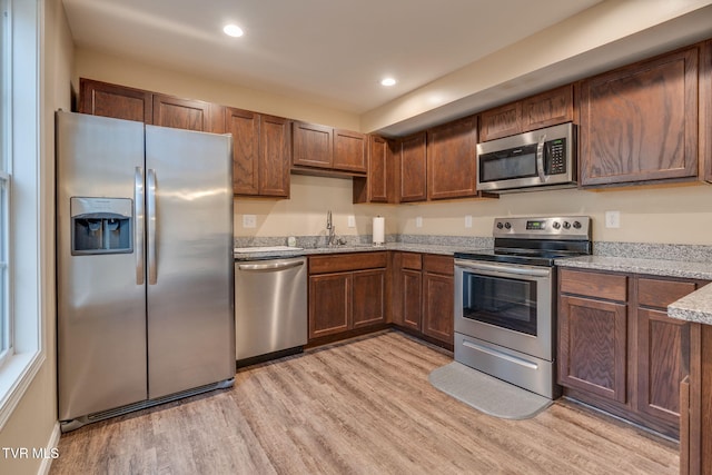 kitchen with light stone countertops, sink, appliances with stainless steel finishes, and light wood-type flooring