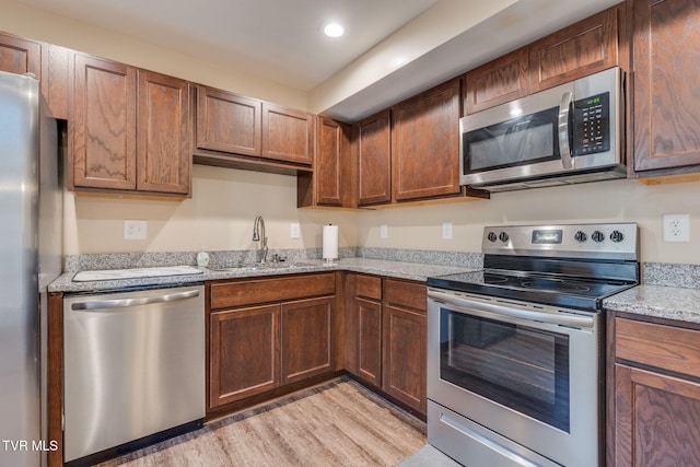 kitchen featuring light wood-type flooring, sink, light stone counters, and stainless steel appliances