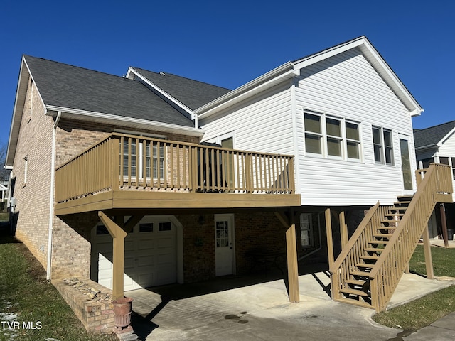 back of property featuring a garage, stairway, roof with shingles, a deck, and brick siding