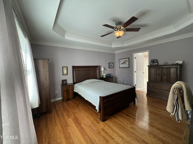 bedroom with a tray ceiling, wood finished floors, a ceiling fan, and crown molding