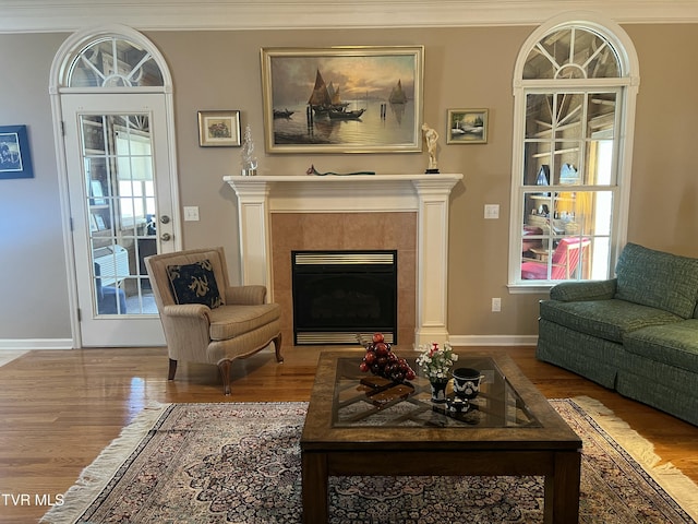 living area with ornamental molding, a tile fireplace, baseboards, and wood finished floors