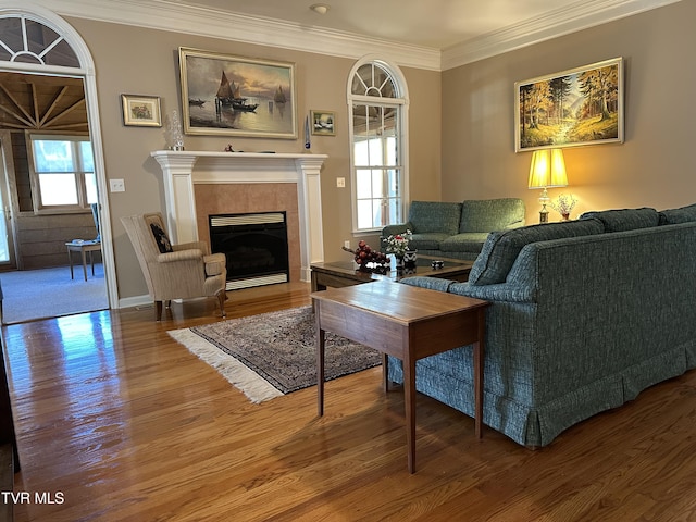 living area featuring a tiled fireplace, ornamental molding, plenty of natural light, and wood finished floors