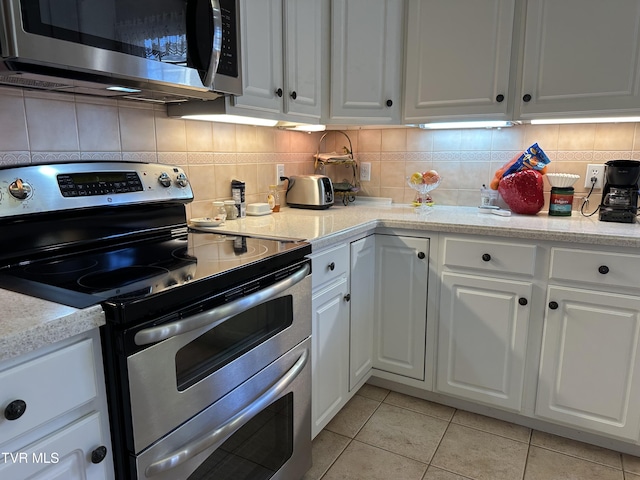 kitchen with appliances with stainless steel finishes, light tile patterned flooring, white cabinets, and tasteful backsplash