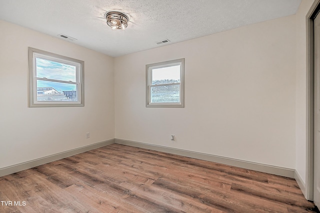 empty room with hardwood / wood-style floors, a textured ceiling, and a healthy amount of sunlight