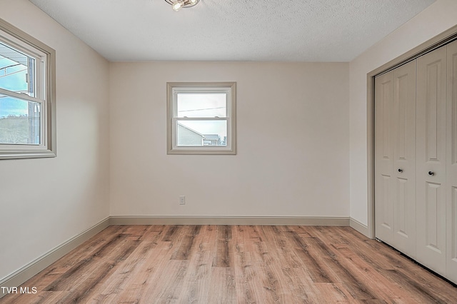 unfurnished bedroom with light hardwood / wood-style floors, a textured ceiling, and a closet