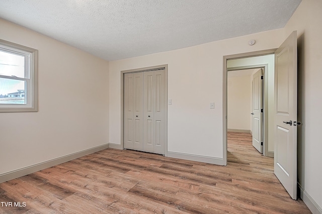 unfurnished bedroom featuring a textured ceiling, a closet, and light hardwood / wood-style flooring