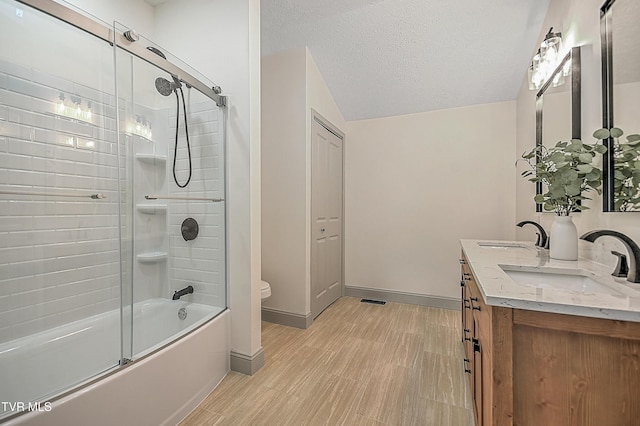 full bathroom featuring bath / shower combo with glass door, a textured ceiling, toilet, and vanity