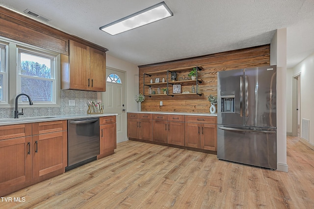 kitchen with decorative backsplash, sink, light wood-type flooring, appliances with stainless steel finishes, and a textured ceiling