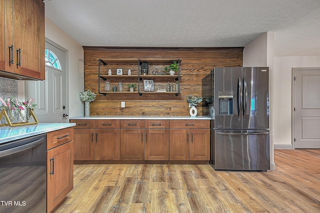 kitchen with dishwasher, light hardwood / wood-style floors, wooden walls, stainless steel fridge with ice dispenser, and a textured ceiling