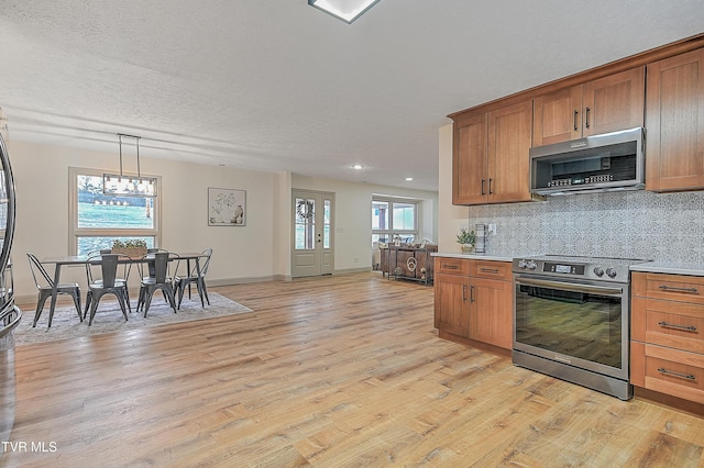 kitchen featuring stainless steel appliances, backsplash, hanging light fixtures, a textured ceiling, and light hardwood / wood-style flooring