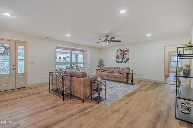 living room with ceiling fan, a textured ceiling, and light hardwood / wood-style flooring