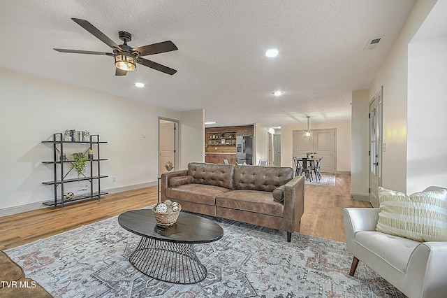 living room featuring ceiling fan, a textured ceiling, and light hardwood / wood-style floors