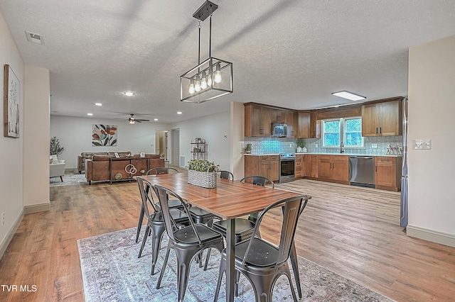 dining area featuring ceiling fan, sink, a textured ceiling, and light hardwood / wood-style flooring