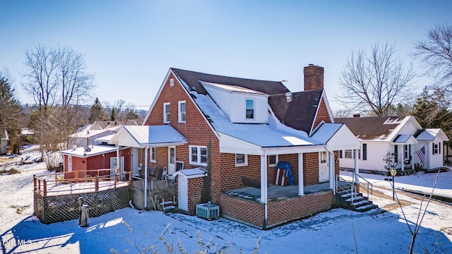 snow covered rear of property with covered porch, a deck, and central AC