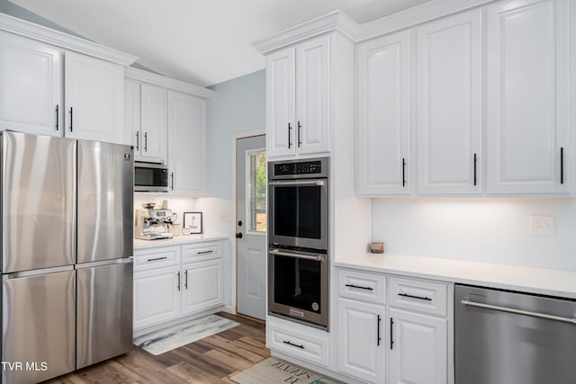 kitchen featuring appliances with stainless steel finishes, white cabinetry, lofted ceiling, and light hardwood / wood-style floors