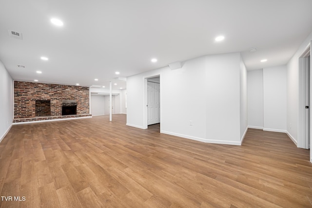 unfurnished living room with light hardwood / wood-style floors, brick wall, and a fireplace