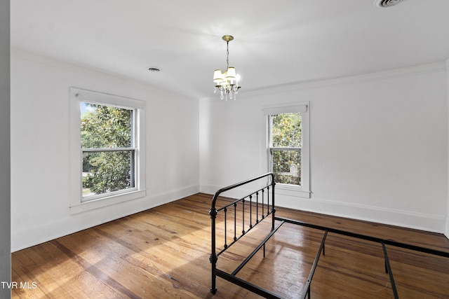 unfurnished room featuring wood-type flooring, an inviting chandelier, and crown molding