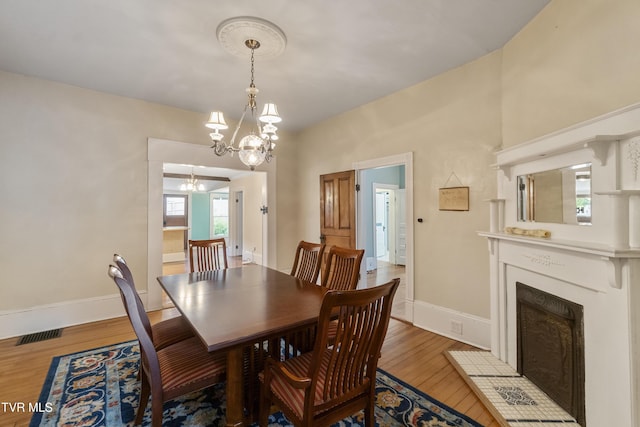 dining room featuring hardwood / wood-style flooring, a tiled fireplace, and a notable chandelier