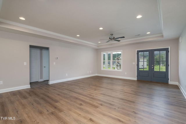 unfurnished living room with wood finished floors, baseboards, a tray ceiling, ornamental molding, and french doors