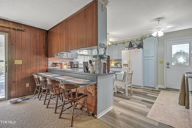 kitchen featuring ceiling fan, a healthy amount of sunlight, white fridge with ice dispenser, and wood walls