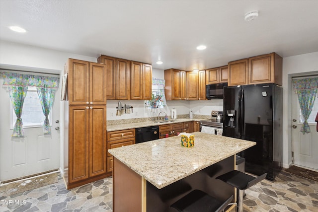 kitchen with sink, light stone counters, a kitchen breakfast bar, a kitchen island, and black appliances