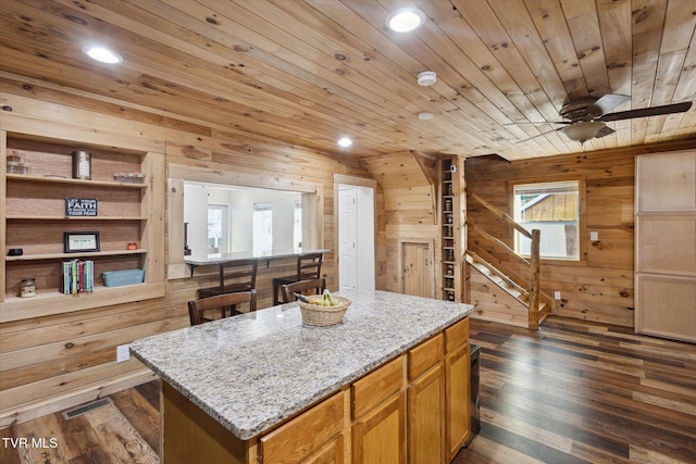 kitchen with light stone counters, wooden walls, ceiling fan, and a kitchen island