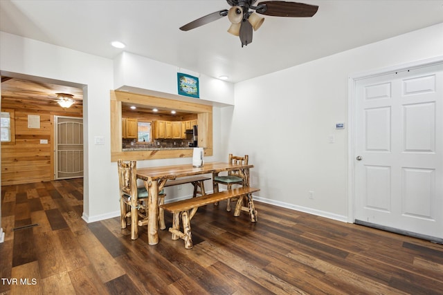 dining space featuring wooden walls, dark wood-type flooring, and ceiling fan