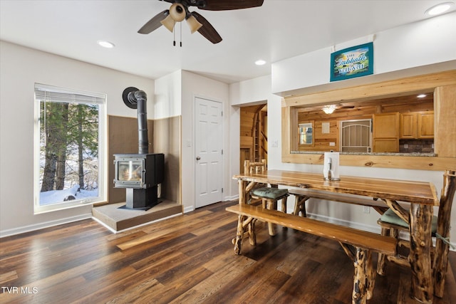 dining room featuring dark wood-type flooring, ceiling fan, and a wood stove