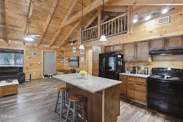 kitchen with wooden walls, a center island, black appliances, wood ceiling, and beam ceiling