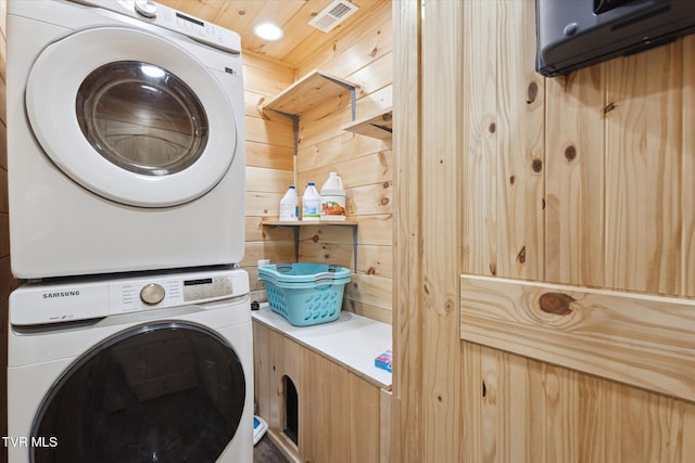 clothes washing area featuring wooden walls and stacked washer / dryer