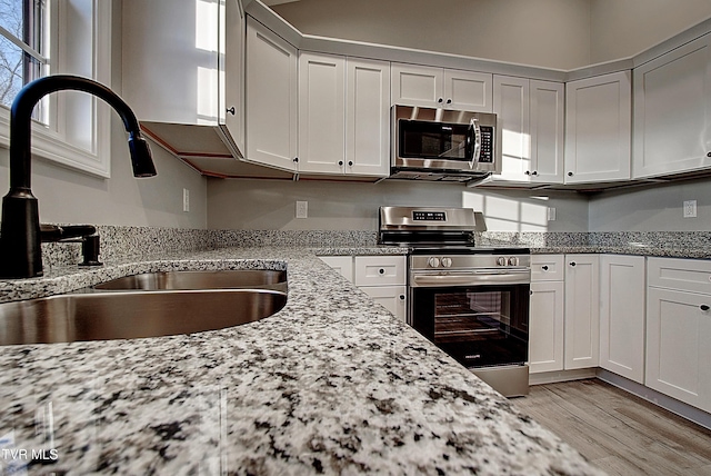 kitchen with sink, stainless steel appliances, white cabinets, and light stone countertops