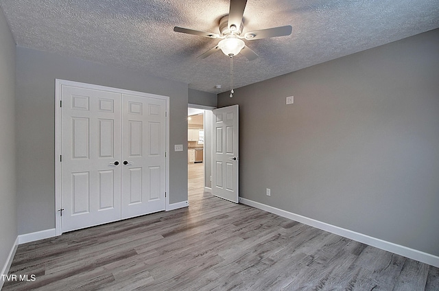 unfurnished bedroom with ceiling fan, light wood-type flooring, a closet, and a textured ceiling