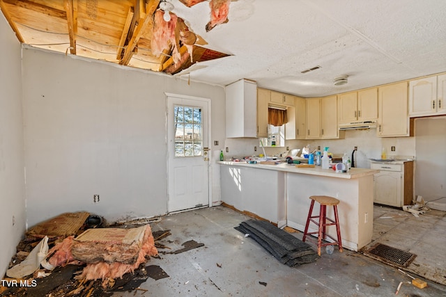 kitchen featuring a textured ceiling, a kitchen breakfast bar, cream cabinets, and kitchen peninsula