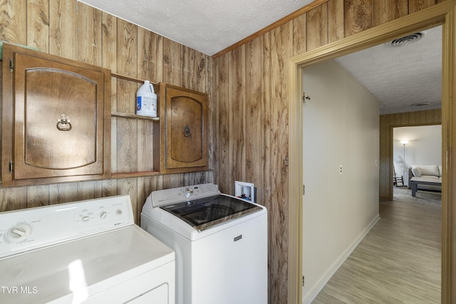 laundry area featuring washer and clothes dryer, wood walls, a textured ceiling, cabinets, and light hardwood / wood-style flooring