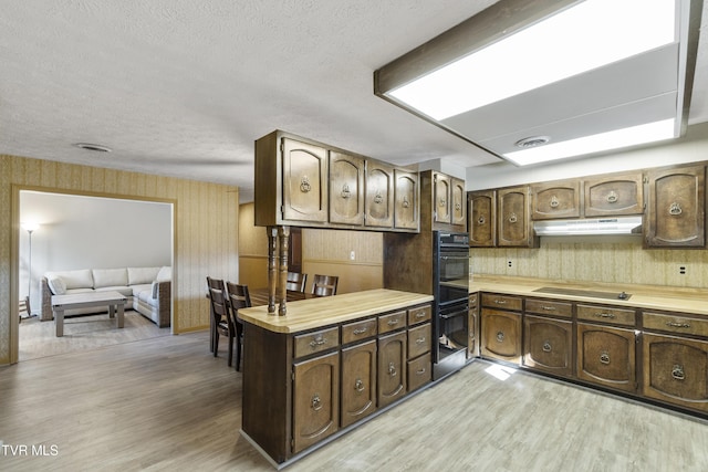 kitchen with kitchen peninsula, dark brown cabinets, light hardwood / wood-style flooring, and black appliances