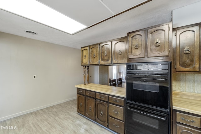 kitchen with black double oven, light hardwood / wood-style floors, and dark brown cabinetry