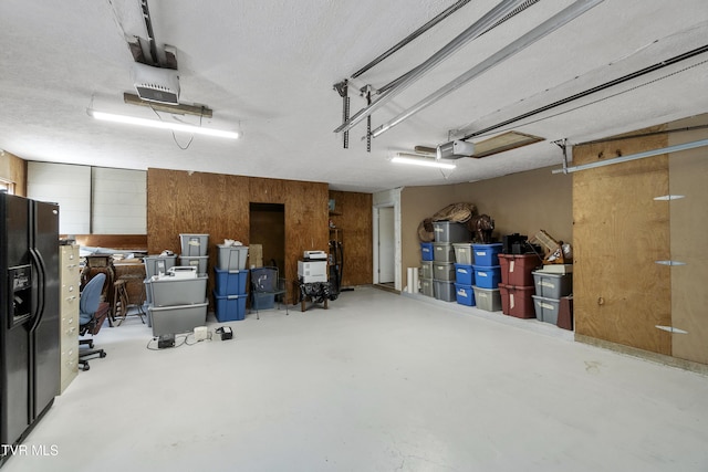 garage with wood walls, black fridge with ice dispenser, and a garage door opener