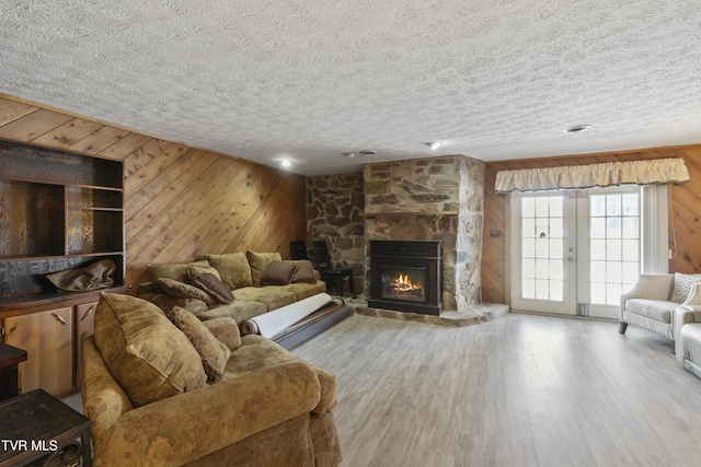 living room featuring wood-type flooring, a fireplace, wood walls, and a textured ceiling