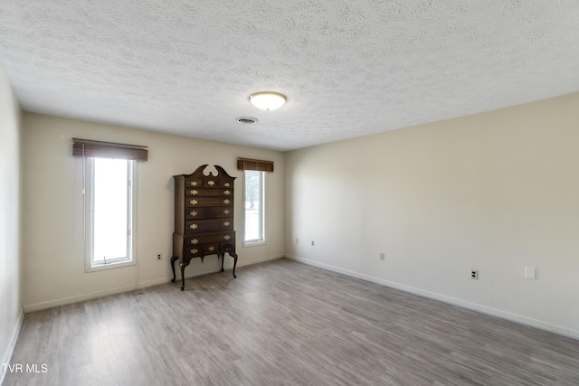 unfurnished room with a textured ceiling, a healthy amount of sunlight, and wood-type flooring