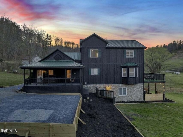 back house at dusk with a porch, a yard, and central air condition unit