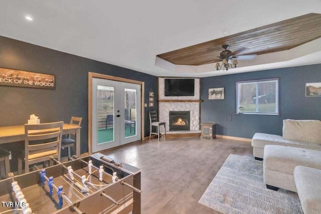 living room featuring french doors, ceiling fan, hardwood / wood-style flooring, and a stone fireplace