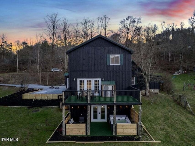 back house at dusk featuring french doors, a lawn, a jacuzzi, and a wooden deck