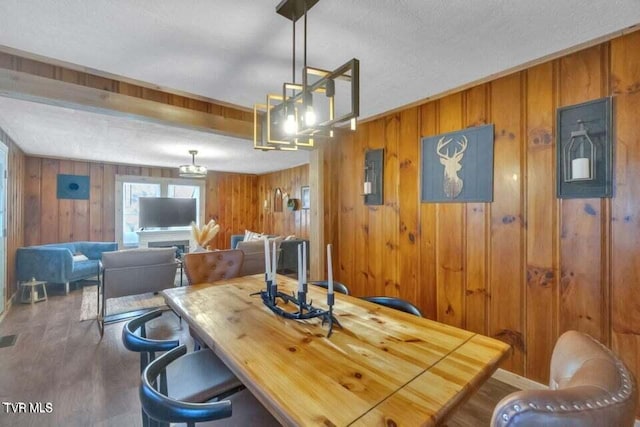 dining area featuring a textured ceiling, wooden walls, and dark hardwood / wood-style flooring